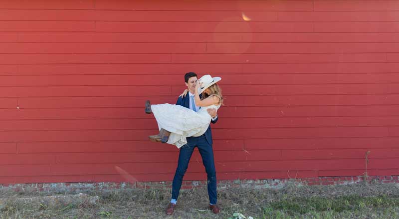 Bride and groom posing against a red barn wall at Hamilton Place Events wedding venue in South Georgia.