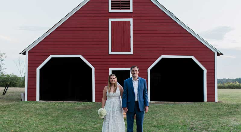 Bride and groom posing in front of rustic red barn wedding venue in South Georgia.