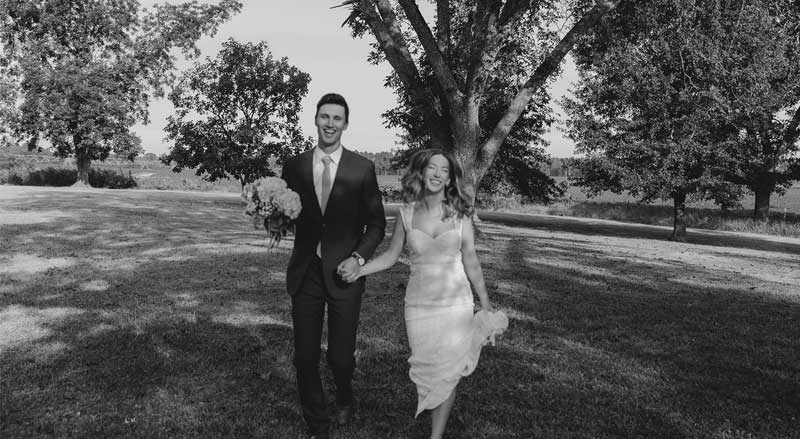 Newlywed couple walking hand in hand under trees at Hamilton Place, showcasing romantic outdoor wedding portraits.